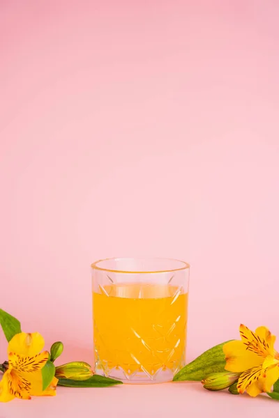 Glass of fresh citrus juice and yellow tropical flowers on pink background — Stock Photo