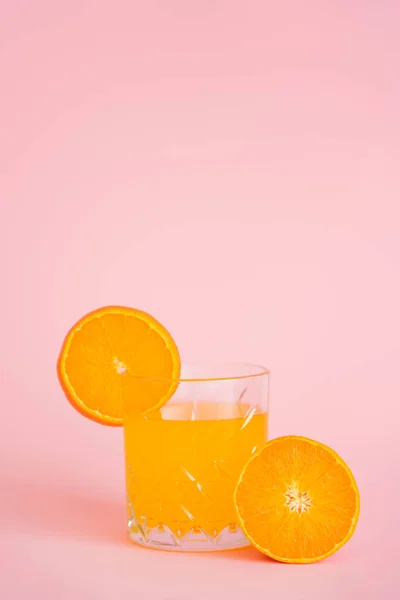 Vidro de suco refrescante e laranja fatiada no fundo rosa — Fotografia de Stock