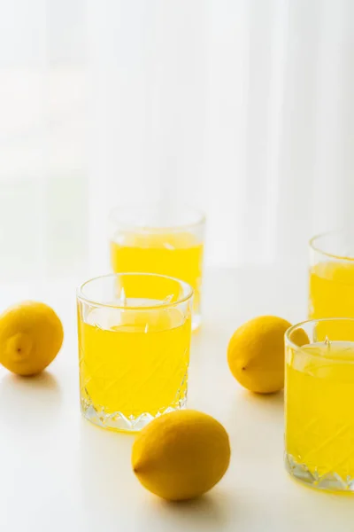 Óculos com limonada natural perto de limões inteiros em fundo branco e borrado — Fotografia de Stock