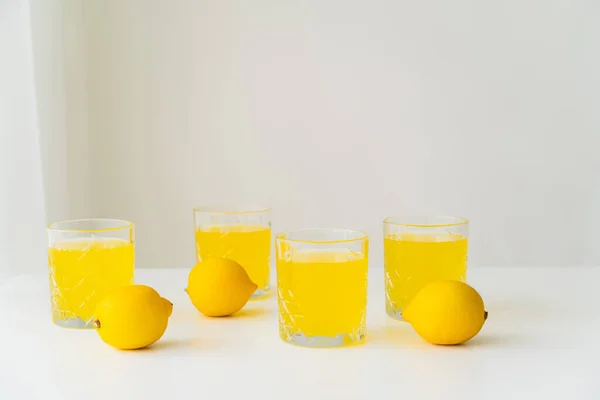 Limões inteiros perto de óculos com suco de citrinos puro em fundo cinza com espaço de cópia — Fotografia de Stock