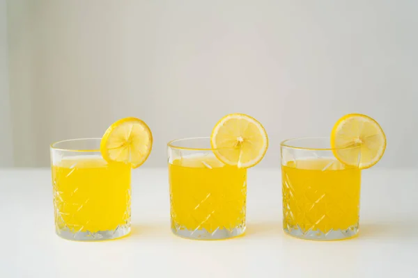 Rodajas de limón fresco sobre vasos con zumo natural de cítricos sobre superficie blanca aislada sobre gris - foto de stock