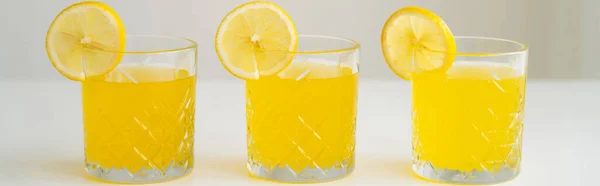 Bicchieri con limonata rinfrescante con fette di limone succoso su superficie bianca isolata su grigio, striscione — Foto stock