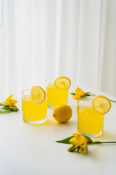 Tónico cítrico fresco cerca de limones y flores de alstroemeria amarillas sobre fondo blanco - foto de stock