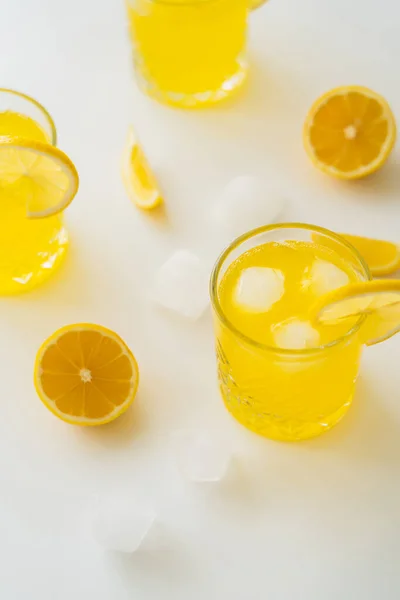 Vista de ángulo alto de vasos con tónico cítrico helado y limones cortados en superficie blanca - foto de stock