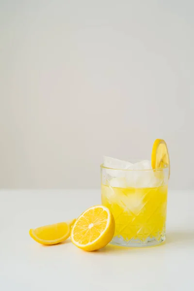 Tonique d'agrumes avec glaçons près de citron coupé sur surface blanche isolé sur gris — Photo de stock