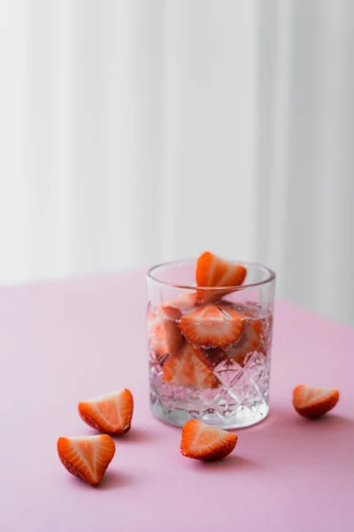 Transparent glass of tonic water with cut strawberries on grey background — Stock Photo