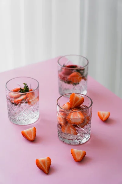 Faceted glasses of tonic water with fresh chopped strawberries on white tabletop — Stock Photo