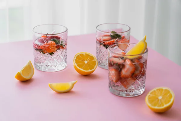 Eau tonique fraîche avec des fraises hachées près de citrons coupés sur le dessus de table blanc — Photo de stock