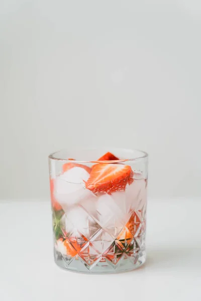 Glass with iced tonic water with chopped strawberries on white surface isolated on grey — Stock Photo