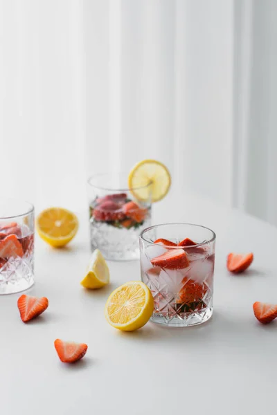 Gläser mit geeistem Erdbeertonikum in der Nähe geschnittener Zitronen auf weißer Tischplatte — Stockfoto