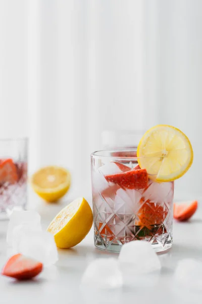 Concentrazione selettiva di acqua tonica con fragole e ghiaccio vicino ai limoni tagliati su fondo bianco sfocato — Foto stock