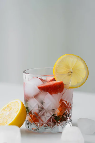 Cold tonic with fresh strawberries and lemon slice on white surface isolated on grey — Stock Photo