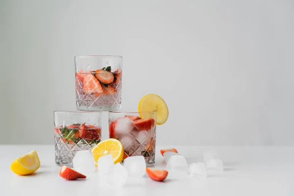 Refrescante bebida tónica con fresas cerca de limones cortados y cubitos de hielo aislados en gris - foto de stock