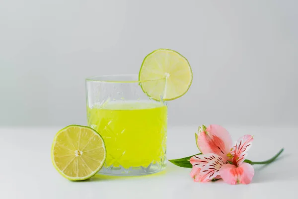 Pink alstroemeria flower and sliced lime near glass of lemonade on white surface isolated on grey — Stock Photo