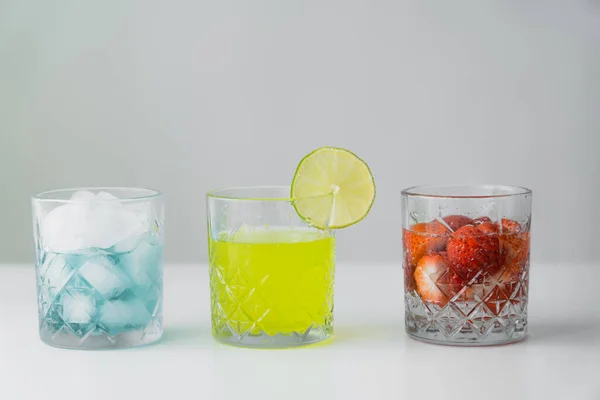 Limonada y tónico fresa cerca de vidrio con cubitos de hielo en la superficie blanca aislado en gris - foto de stock