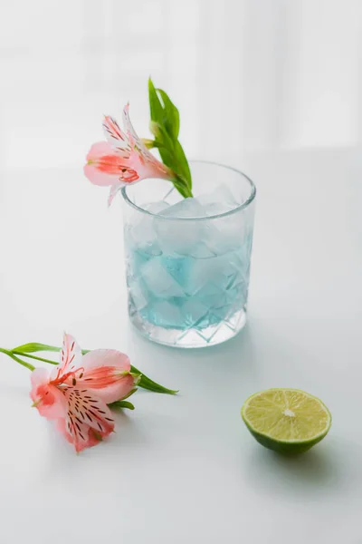 Glas mit eiskaltem Tonic Water in der Nähe von rosa Alstroemeria-Blüten und Limette auf weißer Oberfläche — Stockfoto