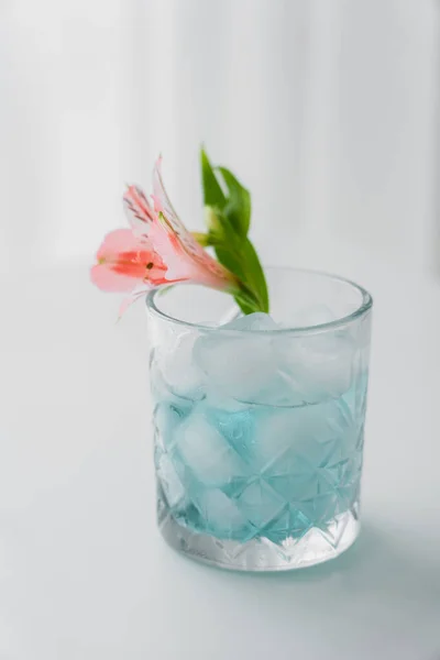 Cristal de vidrio con flor de alstroemeria rosa y bebida tónica helada sobre fondo blanco - foto de stock
