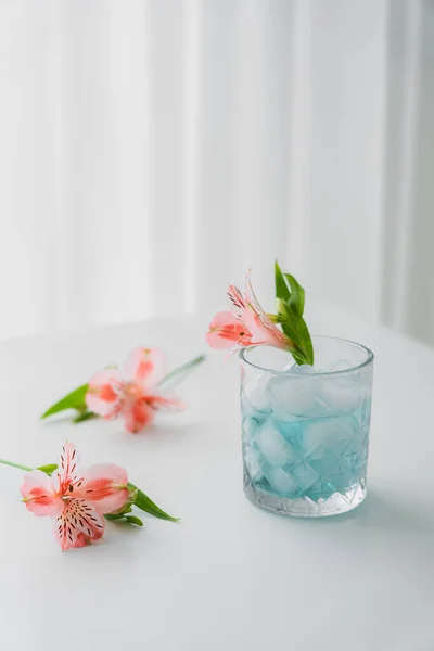 Vetro con freddo tonico e rosa alstroemeria fiore su tavolo bianco e sfondo grigio — Foto stock