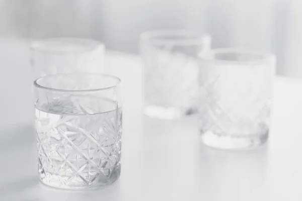 Selective focus of faceted glass with water on white surface and blurred background — Stock Photo