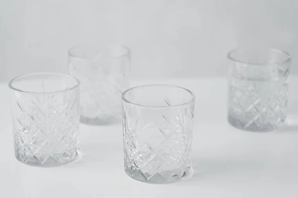 Empty faceted crystal glasses on white tabletop isolated on grey — Stock Photo