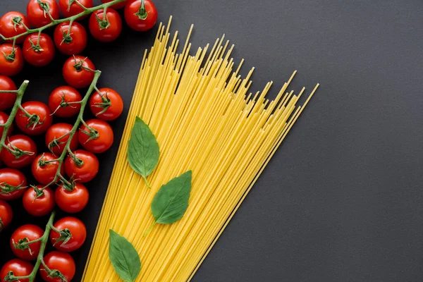 Vista superior de tomates cereja maduros perto de espaguete e manjericão sobre fundo preto — Fotografia de Stock