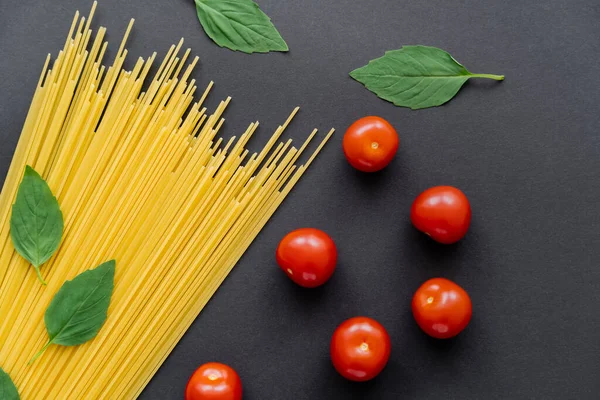 Lavaggi di basilico fresco vicino a pasta cruda e pomodorini su fondo nero — Foto stock