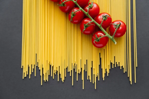 Top view of raw cherry tomatoes on uncooked pasta on black background — Stock Photo