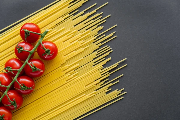 Top view of ripe cherry tomatoes on raw pasta on black background — Stock Photo
