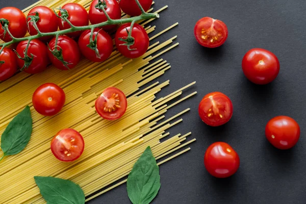 Top view of basil and cherry tomatoes on uncooked pasta on black background — Stock Photo