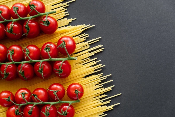 Flat lay de tomate cereja vermelho maduro espaguete cru no fundo preto — Fotografia de Stock