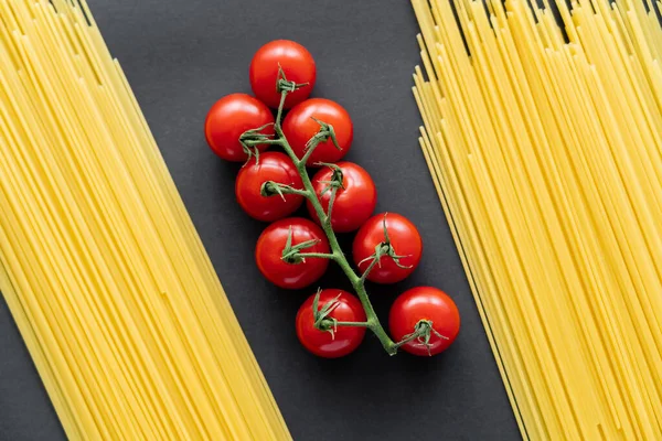 Vue du dessus des tomates cerises sur branche entre spaghettis crus sur fond noir — Photo de stock