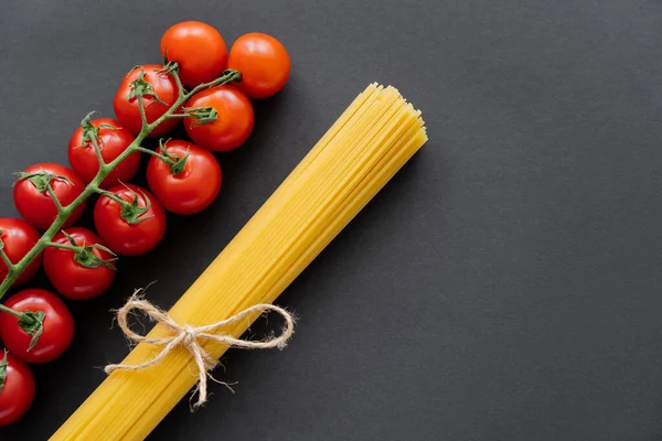 Vista superior de macarrão cru e tomate cereja em fundo preto — Fotografia de Stock