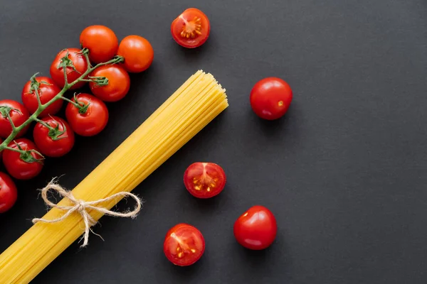 Vista superior de tomates cereja orgânicos e espaguete cru no fundo preto — Fotografia de Stock