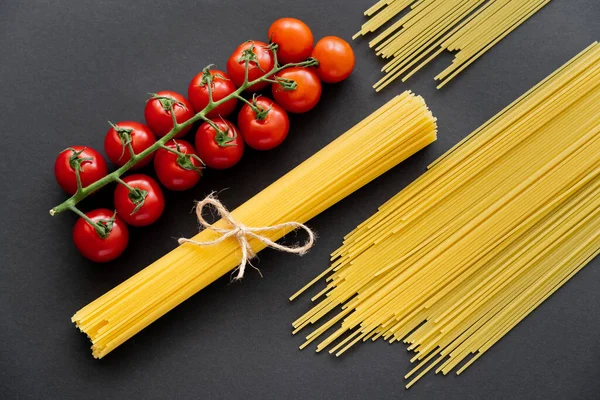 Vue du dessus des pâtes non cuites et des tomates cerises sur fond noir — Photo de stock