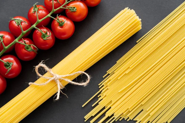 Top view of natural cherry tomatoes and uncooked pasta on black background — Stock Photo