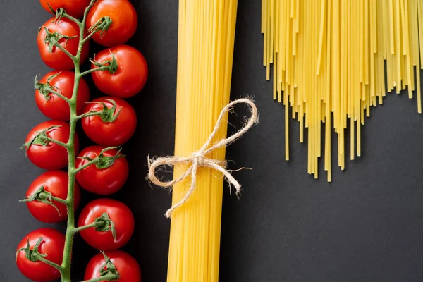 Top view of raw spaghetti and cherry tomatoes on black background — Stock Photo