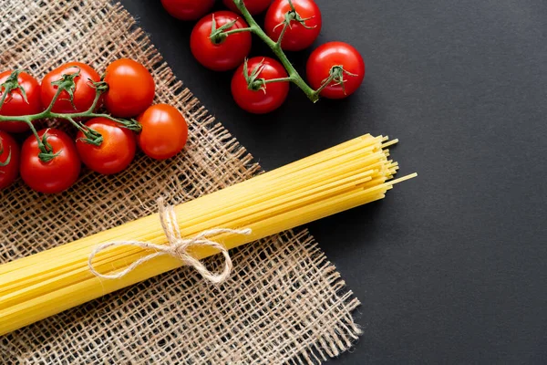 Vue du dessus des spaghettis crus et des tomates cerises sur sac sur fond noir — Photo de stock