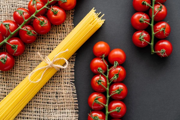 Vista superior de pasta cruda y tomates cherry sobre tela de saco sobre fondo negro - foto de stock