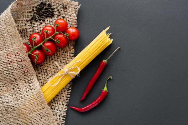 Draufsicht auf Kirschtomaten und Chilischoten in der Nähe von Spaghetti auf Sacktuch auf schwarzem Hintergrund — Stockfoto