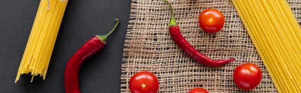 Draufsicht auf natürliches Gemüse und rohe Spaghetti auf Sacktuch auf schwarzem Hintergrund, Banner — Stockfoto