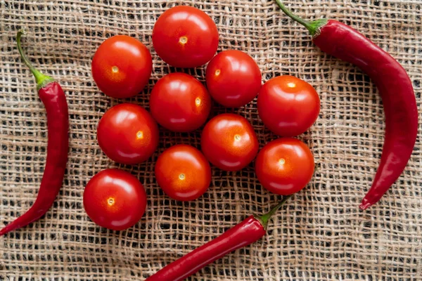 Top view of chili peppers and cherry tomatoes on sackcloth — Stock Photo