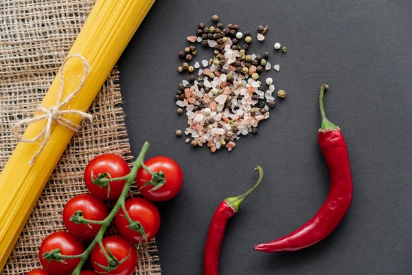 Draufsicht auf ungekochte Spaghetti in der Nähe von Gemüse und Salz auf Sacktuch auf schwarzem Hintergrund — Stockfoto