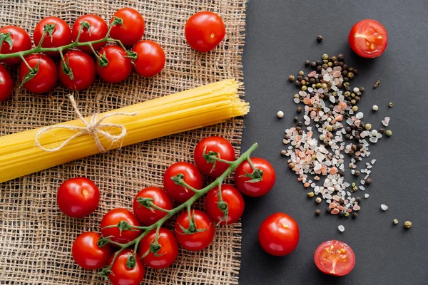 Top view of vegetables near spices and raw spaghetti on sackcloth on black background — Stock Photo