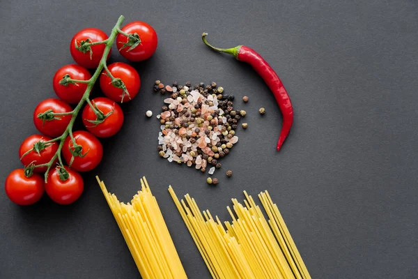 Draufsicht auf ungekochte Pasta in der Nähe von Gewürzen und frischem Gemüse auf schwarzem Hintergrund — Stockfoto