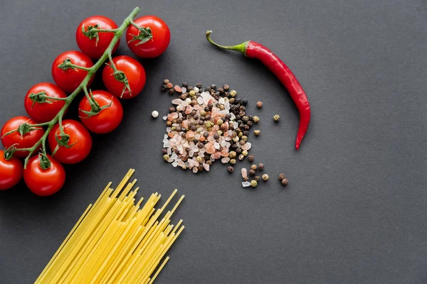 Top view of raw pasta near spices and vegetables on black background — Stock Photo