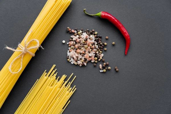 Top view of chili pepper near spices and raw spaghetti on black background — Stock Photo