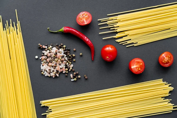 Top view of vegetables with raw spaghetti and spices on black background — Stock Photo