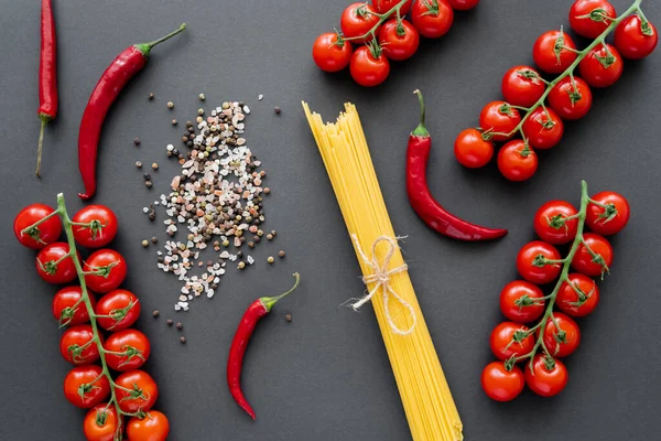 Vista dall'alto di pasta cruda vicino a verdure rosse e spezie su sfondo nero — Foto stock