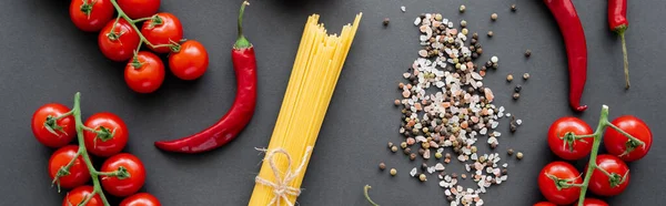 Draufsicht auf rotes reifes Gemüse in der Nähe roher Pasta und Gewürze auf schwarzem Hintergrund, Banner — Stockfoto