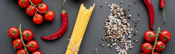 Top view of red ripe vegetables near raw pasta and spices on black background, banner — Stock Photo